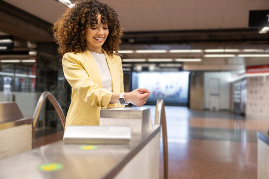 Smiling woman using smartwatch at train station turnstile
