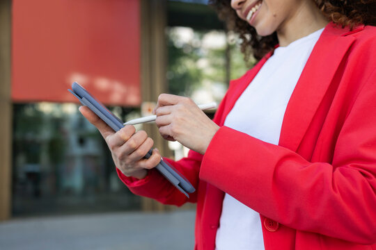 Hispanic woman in red blazer using tablet outdoors