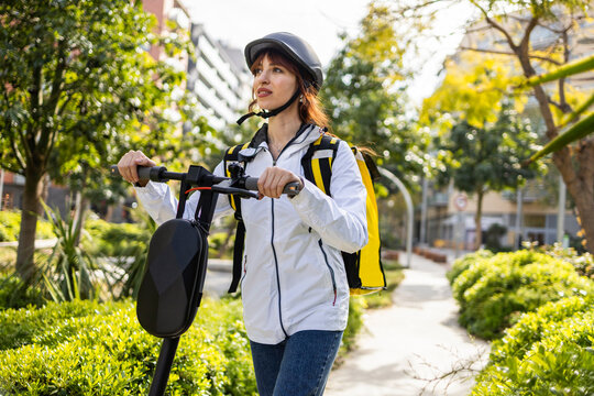Female delivery rider with backpack on scooter in city park