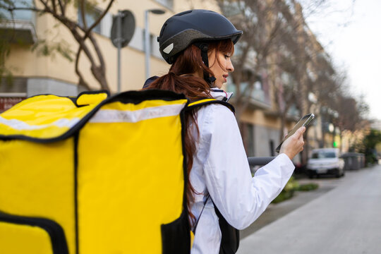 Female food delivery rider checking smartphone on city street