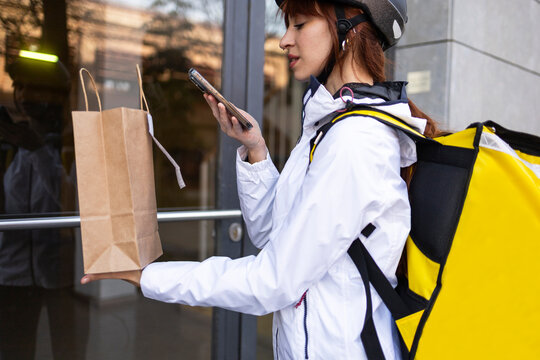 Female food delivery rider checking phone at doorstep
