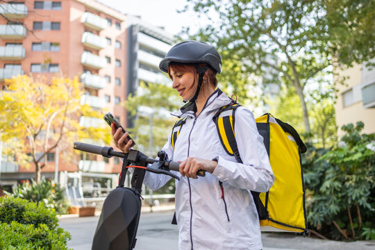 Female food delivery rider checking phone by scooter