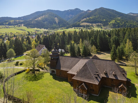 Aerial view of the Wooden Articular Church of Svaty Kriz surrounded by green meadows and dense forests with mountains in the background in Svaty Kriz, Zilinsky kraj, Slovakia.