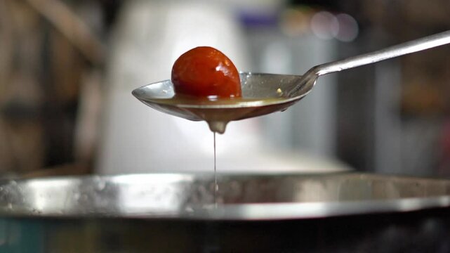 Macro Shot of Juicy Indian Gulab Jamun Dripping with Sugar Syrup on a Spoon. Traditional Indian Sweet Dessert Gulab Jamun Served Hot in a Commercial Kitchen. Indian Mithai Gulab Jamun Preparation.
