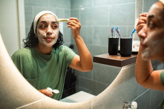 Woman applying face mask in home bathroom mirror