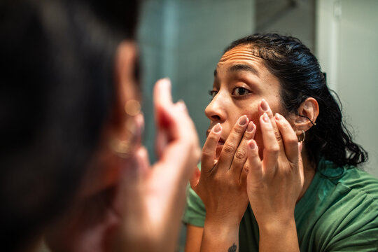 Woman checking her skin in bathroom mirror