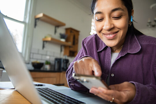 Smiling woman using smartphone and laptop at home