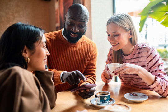 Three friends looking at smartphone and drinking coffee in a cafe