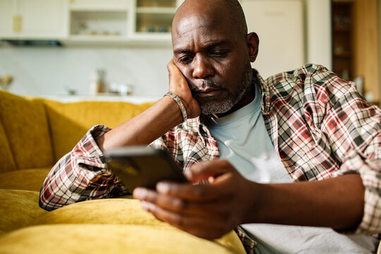 Middle-aged man checking smartphone on yellow sofa at home