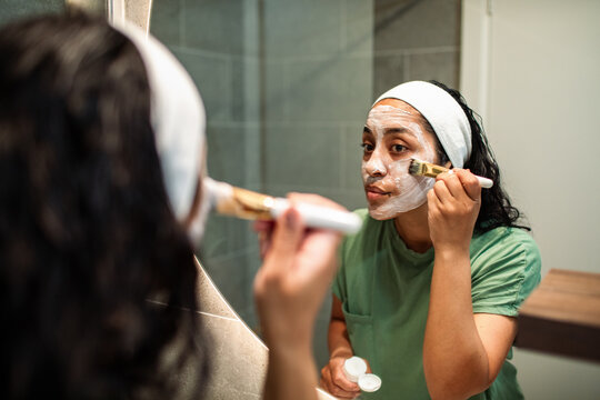 Woman applying facial mask with brush in bathroom mirror