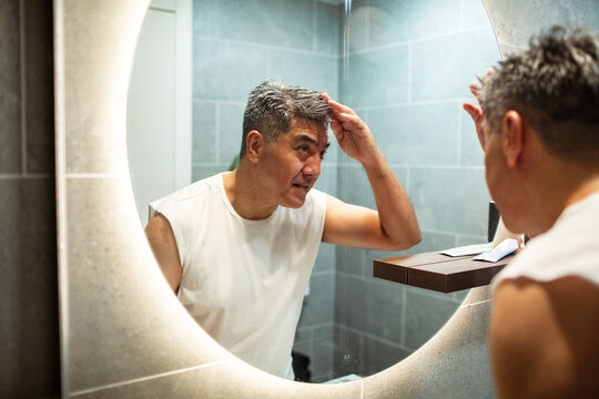 Middle-aged man checking hair in bathroom mirror at home