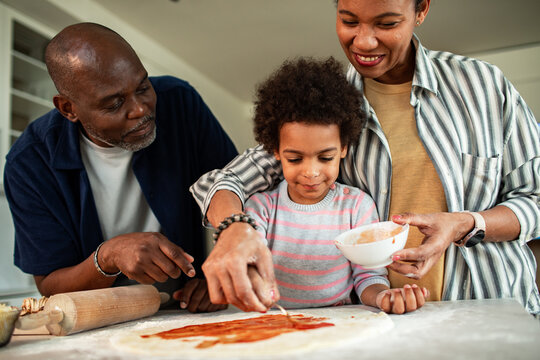 Parents help child make homemade pizza in kitchen