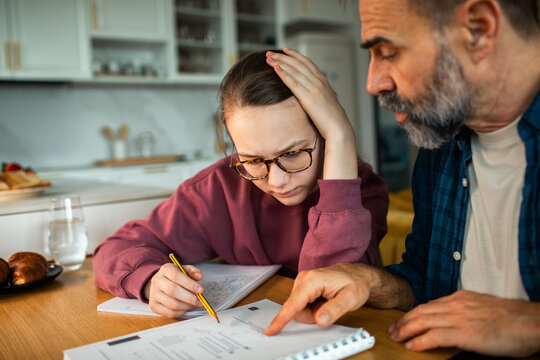Father helping teenage daughter with homework at kitchen table