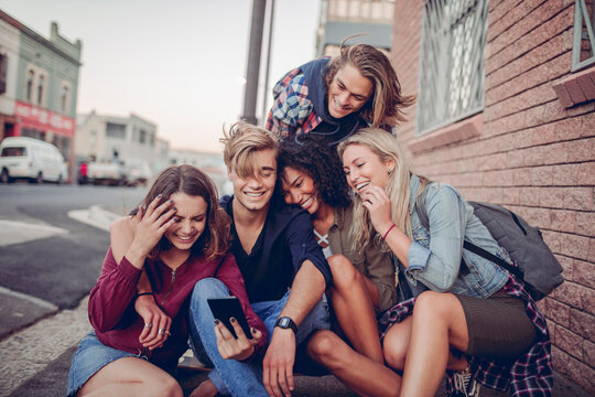 Diverse friends laughing at smartphone on city sidewalk
