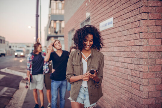Young friends walking in city street, woman smiling at smartphone