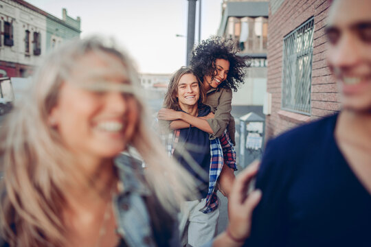 Friends laughing and piggyback ride in city street