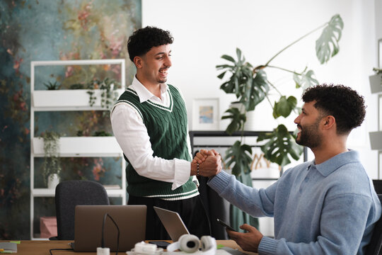 Two men shake hands in a modern office setting, celebrating a successful collaboration.
