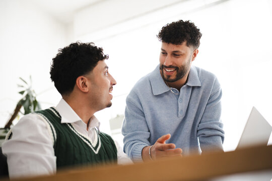 Two young men are engaged in a conversation, one gesturing with his hand while the other listens attentively.