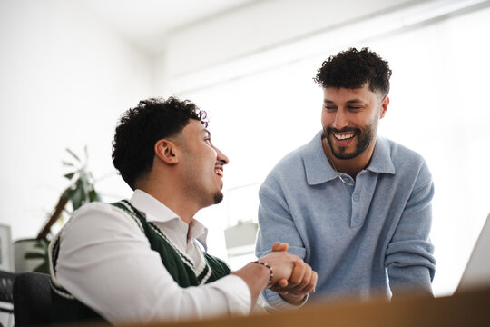 Two men are smiling and talking while working together in an office setting.