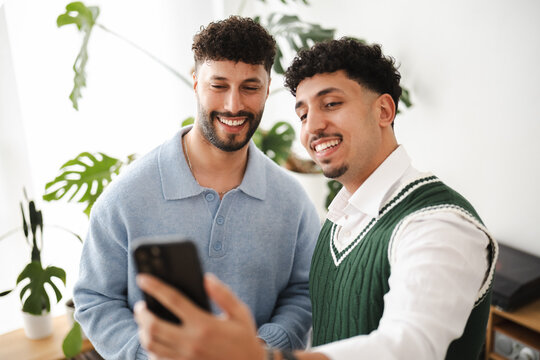 Two young men smile while looking at a smartphone together, sharing a moment of connection and digital interaction.