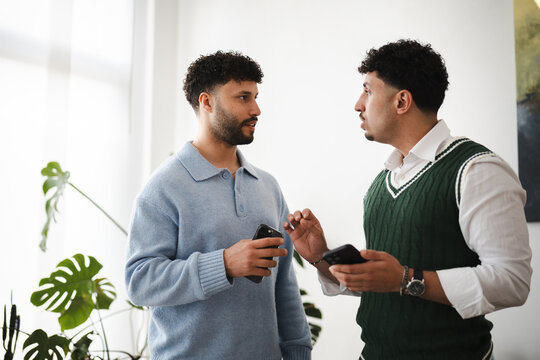 Two young men are engaged in a conversation while holding their phones, suggesting a discussion about technology or a shared digital experience.