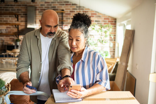 Mature couple planning home move with smartphone in kitchen