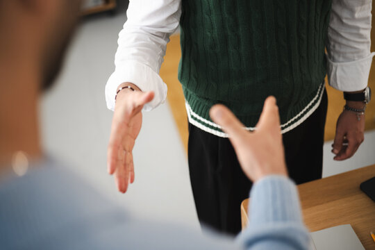 Two people are shaking hands, one wearing a white shirt and green sweater vest, the other in a blue sweater, signifying agreement or a greeting.