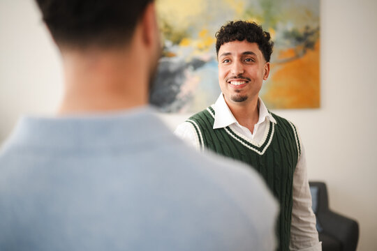 Two men are in conversation, one facing the camera with a smile, the other with his back to the viewer.