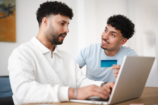 Two men are looking at a laptop, one holding a credit card, suggesting online shopping or financial planning.