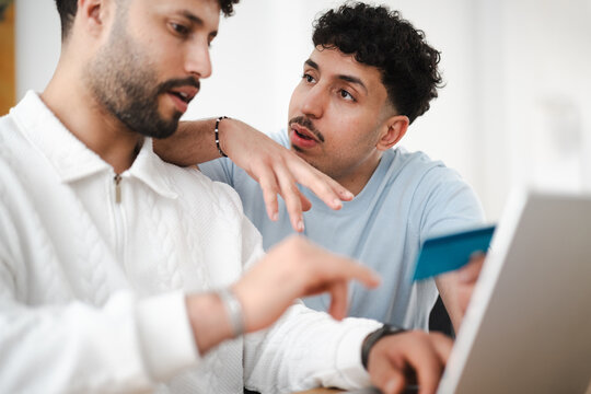Two men are looking at a laptop and holding a credit card, suggesting online shopping or financial planning.