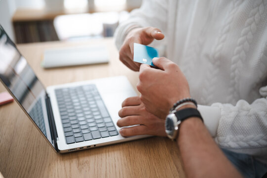 A person hands a credit card to another person over a laptop, symbolizing online payment or financial transaction.