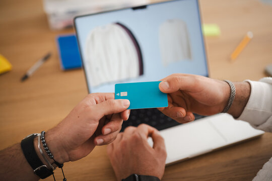 A person holds a credit card over a laptop, ready to make an online purchase of clothing displayed on the screen.