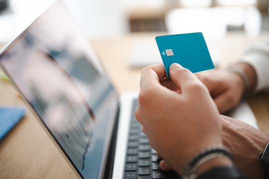 A person holds a credit card near a laptop, ready to make an online purchase. This image represents digital transactions and modern commerce.
