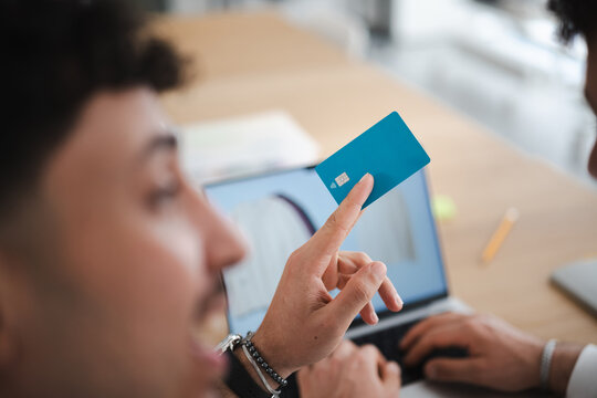 A man holds a debit card while another person types on a laptop, suggesting online banking or a transaction.