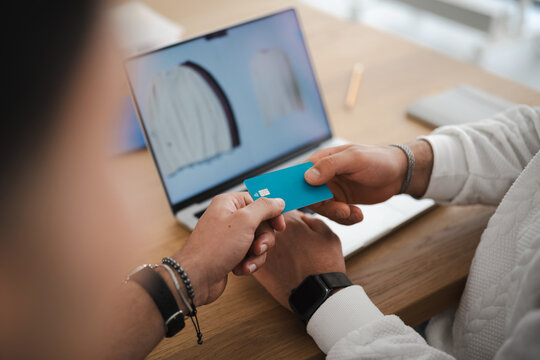 Two people are shown exchanging a payment card in front of a laptop displaying an online shopping page.