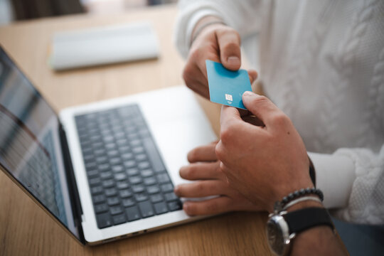 A person is holding a credit card near a laptop, ready to make an online purchase.