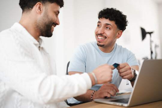 Two men are smiling and interacting with a credit card and a laptop, suggesting a transaction or financial discussion.