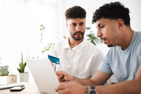 Two men are looking at a laptop and holding a credit card, suggesting online shopping or financial planning.