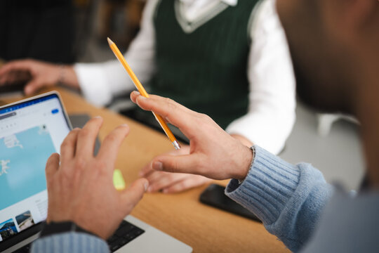 Two people collaborate on a project, one pointing with a pencil at a laptop screen displaying a map.