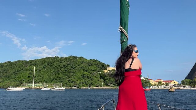 Elegant woman caucasian brunette on sailboat with tropical coastal landscape, pan to the right camera, in Brazil near Sugarloaf Mountain