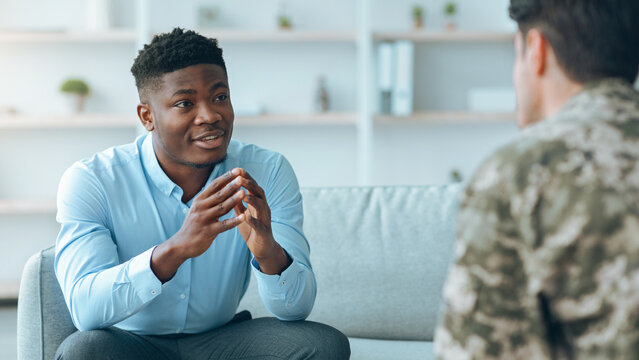 Two men are engaged in a discussion in a simple indoor space. One man wears a blue shirt and speaks with hand gestures while the other listens attentively. Their conversation appears meaningful.
