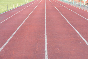 Fototapeta premium Red running track features clearly marked lanes with a green grass field visible in the background, suitable for athletic training and events