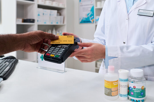 Close up of customer paying by credit card at pharmacy counter, pharmacist processing contactless transaction for prescription purchase. Ideal for healthcare retail and payment services