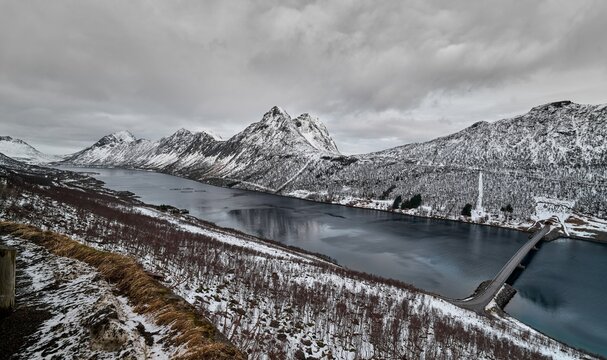 Scenic view of the bridge crossing the fjord near Gryllefjord in Senja, northern Norway, surrounded by dramatic mountains, Arctic coastline and moody Nordic landscape beneath dark clouds.