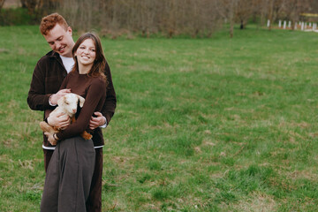 Obraz premium Joyful couple outdoors with a goat kid, embracing in a grassy field, warm sun, relaxed pose, candid moment, natural colors, rural backdrop, simple happiness, wholesome lifestyle