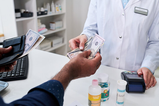 Close up of pharmacist receiving cash from customer at pharmacy counter, processing medication purchase and healthcare payment. Useful for insurance, prescription costs, retail care