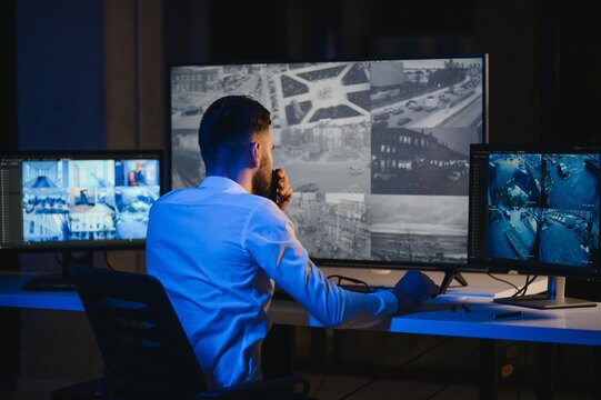 Back view of man watching surveillance footage and map on computers