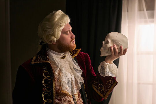 Young man wearing historical costume holding skull and contemplating mortality, referencing Hamlet. Useful for theater promotion, literature education, drama concepts