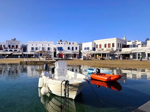 Photo of traditional whitewashed buildings and colorful fishing boats moored along Akti Kampani street at the charming Old Port of Mykonos island, Greece.