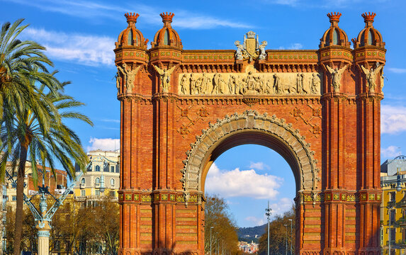 Triumphal Arch in Barcelona, Catalonia, Spain. Arc de Triomf at boulevard street. Alley with tropical palm trees. Early morning landscape with shadows and blue sky with clouds. Famous landmark..